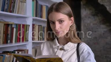 年轻严肃的女孩正在看书，在镜头前看书，在后台看图书馆